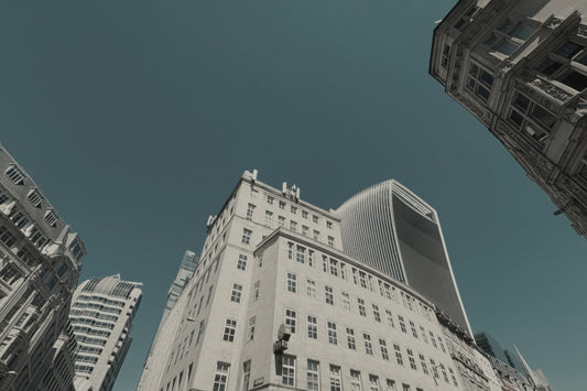 Low-angle photograph of tall city buildings against a muted teal-blue sky, with one large light-colored building centered and other structures framing the edges.