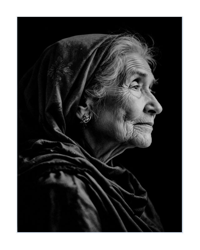 Black and white portrait print of an elderly woman in profile wearing a draped headscarf, shown against a dark background with a white border around the artwork.