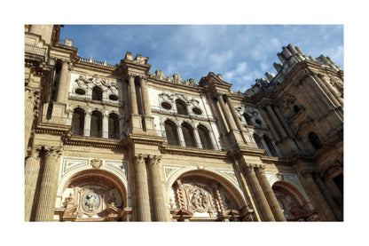 A low-angle photograph of the ornate stone facade of a historic cathedral, featuring columns, arches, and sculpted details under a blue sky with light clouds.