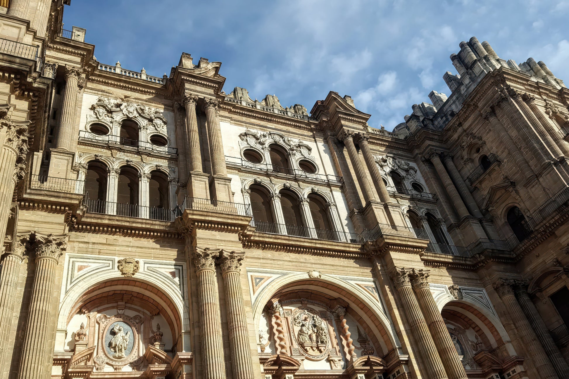 The grand facade of a historic cathedral with ornate stone carvings, columns, and arched windows under a blue sky with light clouds.