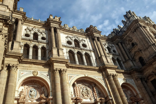 The grand facade of a historic cathedral with ornate stone carvings, columns, and arched windows under a blue sky with light clouds.