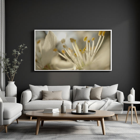 A large horizontal framed wall art print featuring a close-up photograph of cream and yellow flower stamens, displayed above a light gray sofa in a modern living room setting.