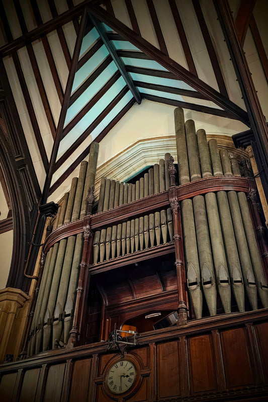 A large historic pipe organ with tall wooden pipes and dark wood casing, photographed inside a church or historic building with exposed wooden ceiling beams and a clock below.