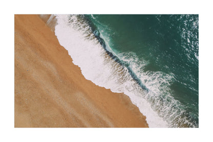 Aerial view of a beach shoreline with tan sand, white surf, and deep teal ocean water, presented as a square print or artwork on a white background.