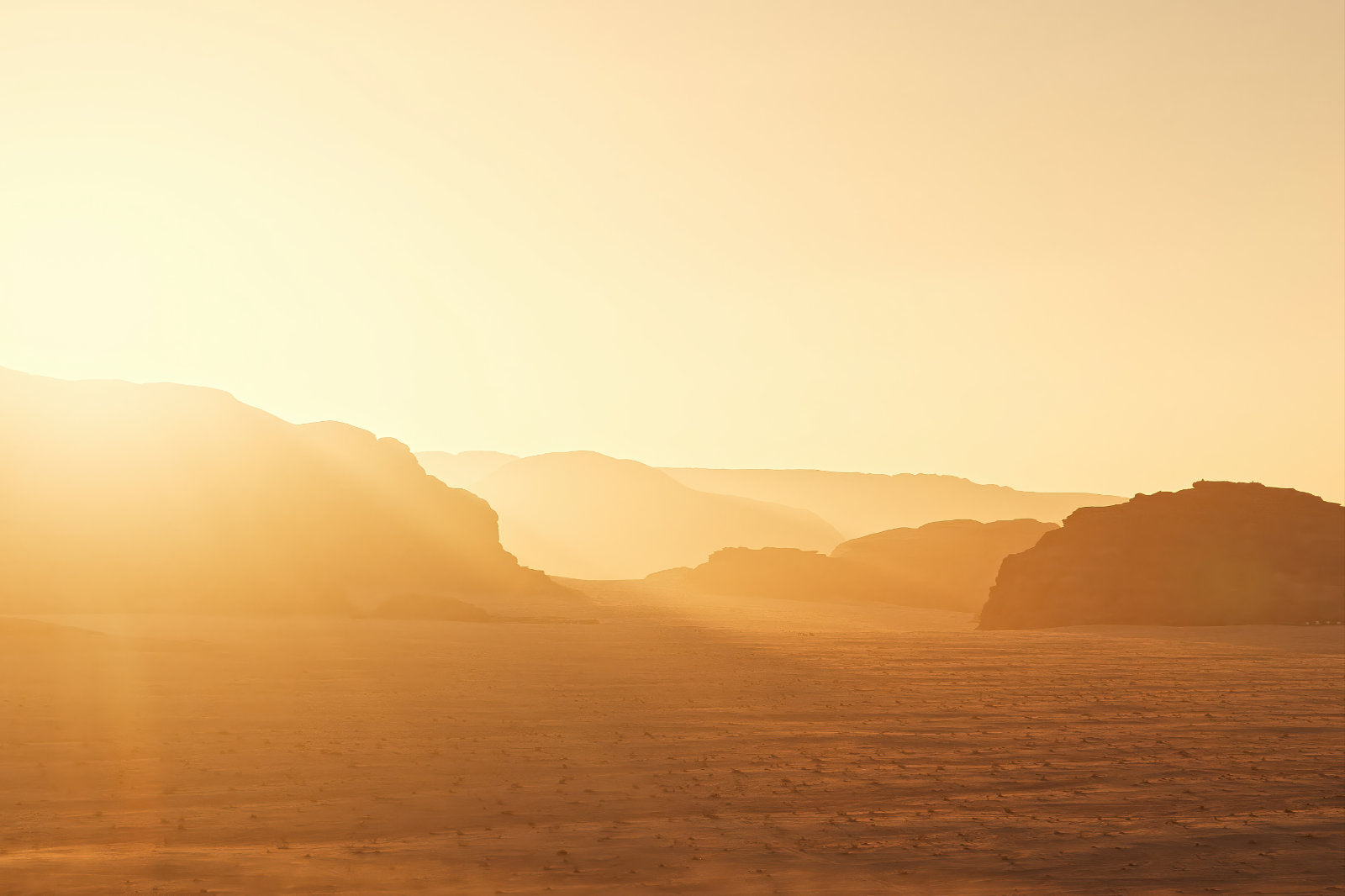 A warm golden desert landscape with layered rock formations in the distance and a bright sunlit sky.