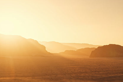 A warm golden desert landscape with layered rock formations in the distance and a bright sunlit sky.