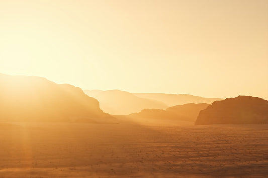 A warm golden desert landscape with layered rock formations in the distance and a bright sunlit sky.
