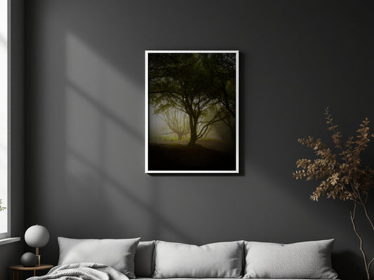 A vertical framed art print depicting a misty forest tree, displayed on a dark gray wall above a modern gray sofa in a styled living room setting.