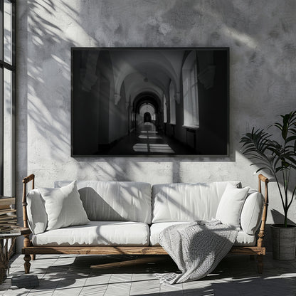A large black and white framed wall art print depicting an arched hallway, displayed above a white sofa in a modern, sunlit room with textured walls and a potted plant.