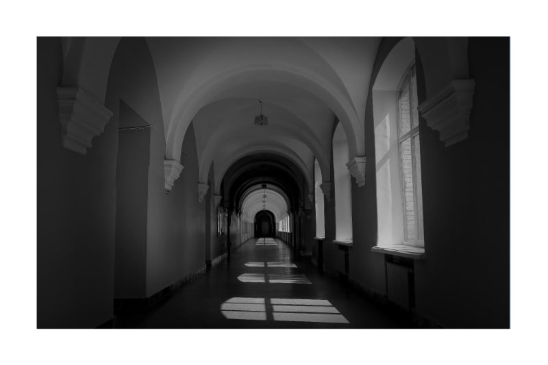 Black and white architectural photograph of a long hallway with arched ceilings and windows casting striped light and shadow on the floor, shown as a square print with a white border.