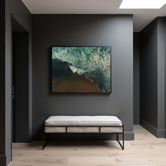A framed abstract ocean wave artwork hangs on a dark gray wall above a light upholstered bench in a modern hallway with pale wood flooring.