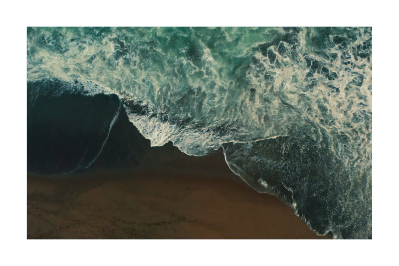 An aerial photograph of ocean waves with white foam crashing onto a sandy beach, presented as a square art print with a white border.
