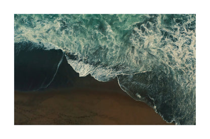 An aerial photograph of ocean waves with white foam crashing onto a sandy beach, presented as a square art print with a white border.