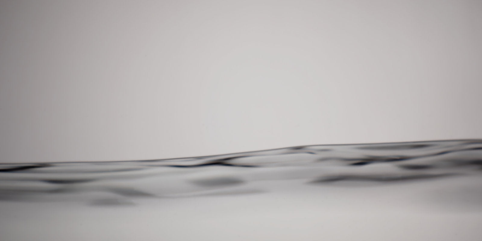 A close-up abstract view of a dark wavy horizontal line or band across a light gray background.