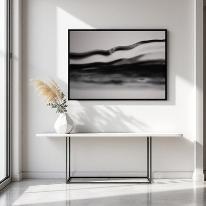 A framed black and white abstract wall art print hangs above a white console table with a vase of pampas grass in a bright, modern interior.