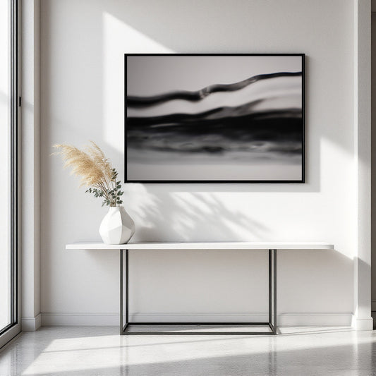 A framed black and white abstract wall art print hangs above a white console table with a vase of pampas grass in a bright, modern interior.