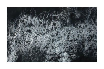 A square photographic print or poster depicting an aerial view of white ocean waves and foam against a dark water background, centered on a white border.