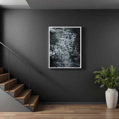 A framed black and white abstract art print hanging on a dark gray wall in a modern interior setting with wooden stairs and a potted plant.