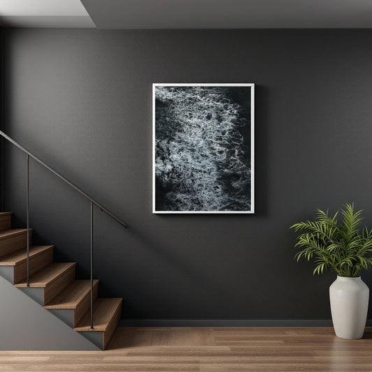 A framed black and white abstract art print hanging on a dark gray wall in a modern interior setting with wooden stairs and a potted plant.