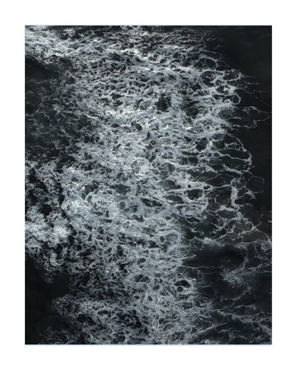 An aerial photograph of dark water with dense white sea foam, presented as a square art print with a white border.