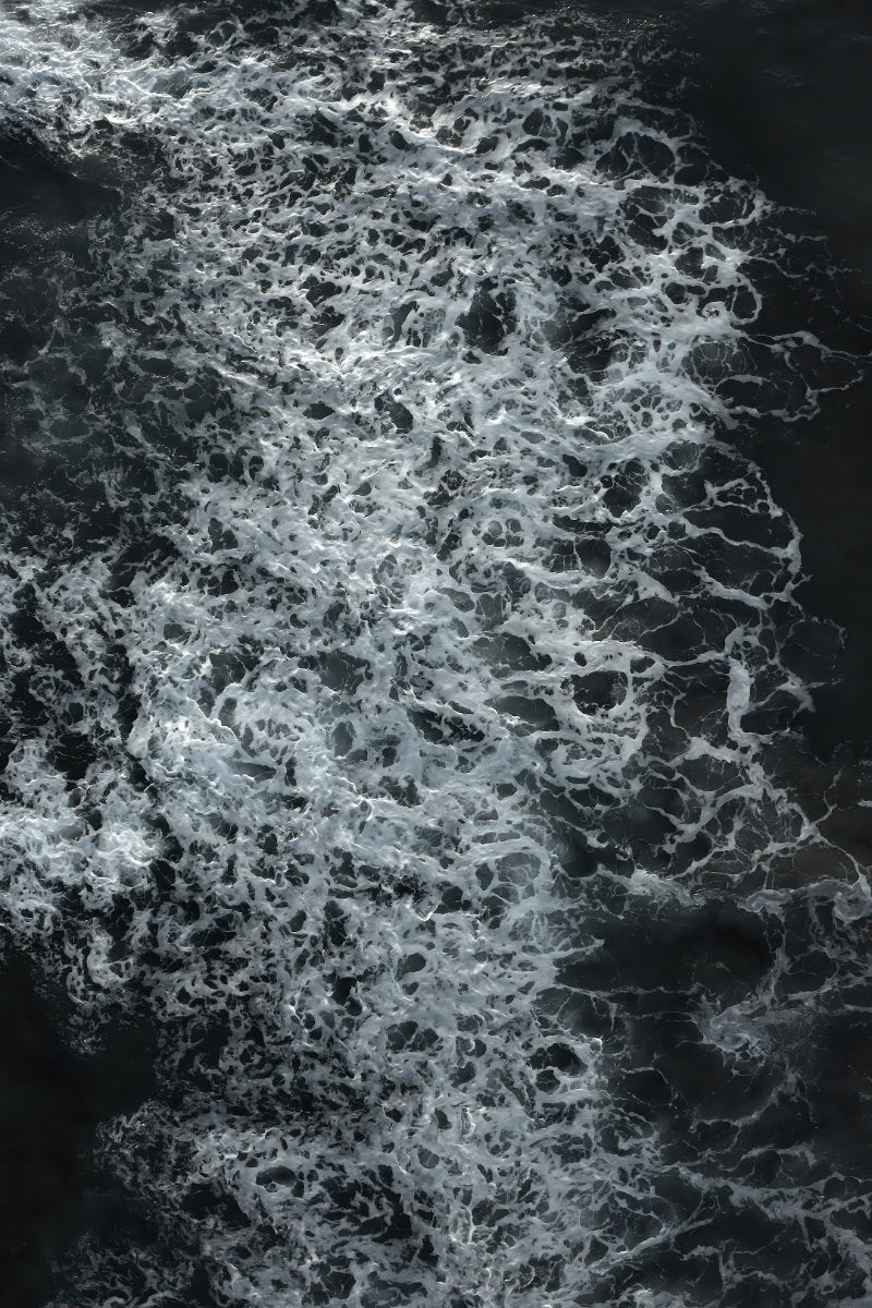 Abstract black and white water texture with dense white foam swirling over dark water.