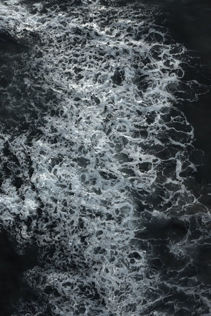 Abstract black and white water texture with dense white foam swirling over dark water.