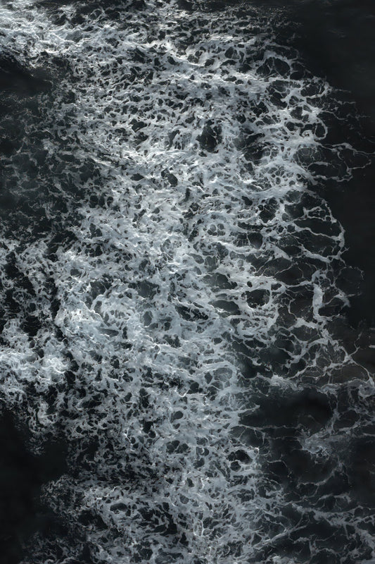 Abstract black and white water texture with dense white foam swirling over dark water.