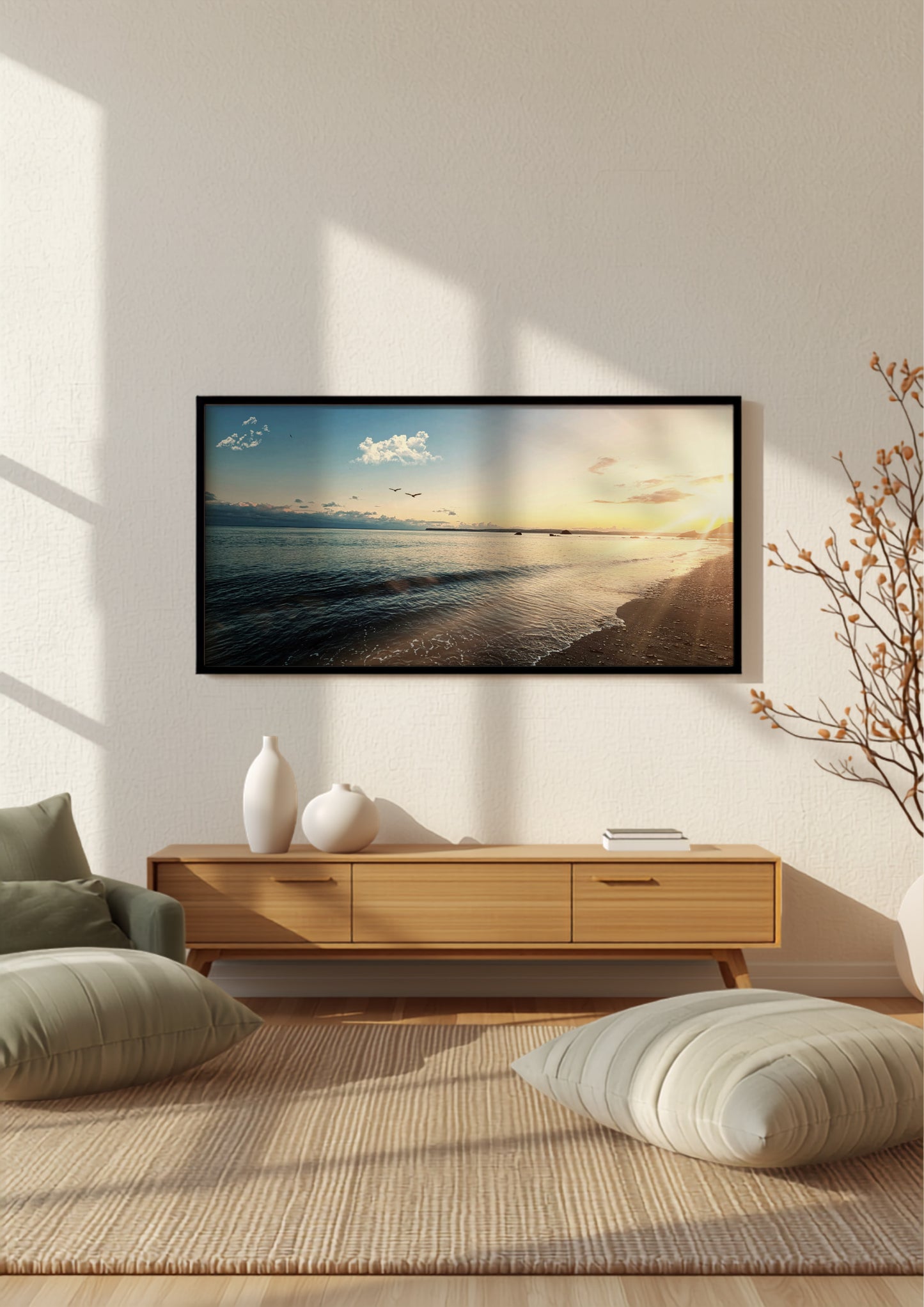 A framed wall art print depicting a beach sunset over calm water, displayed in a modern living room setting above a light wood console table with decorative vases and cushions.